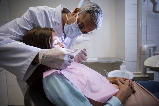 A dentist performs a dental exam on a female patient using examination tools. 